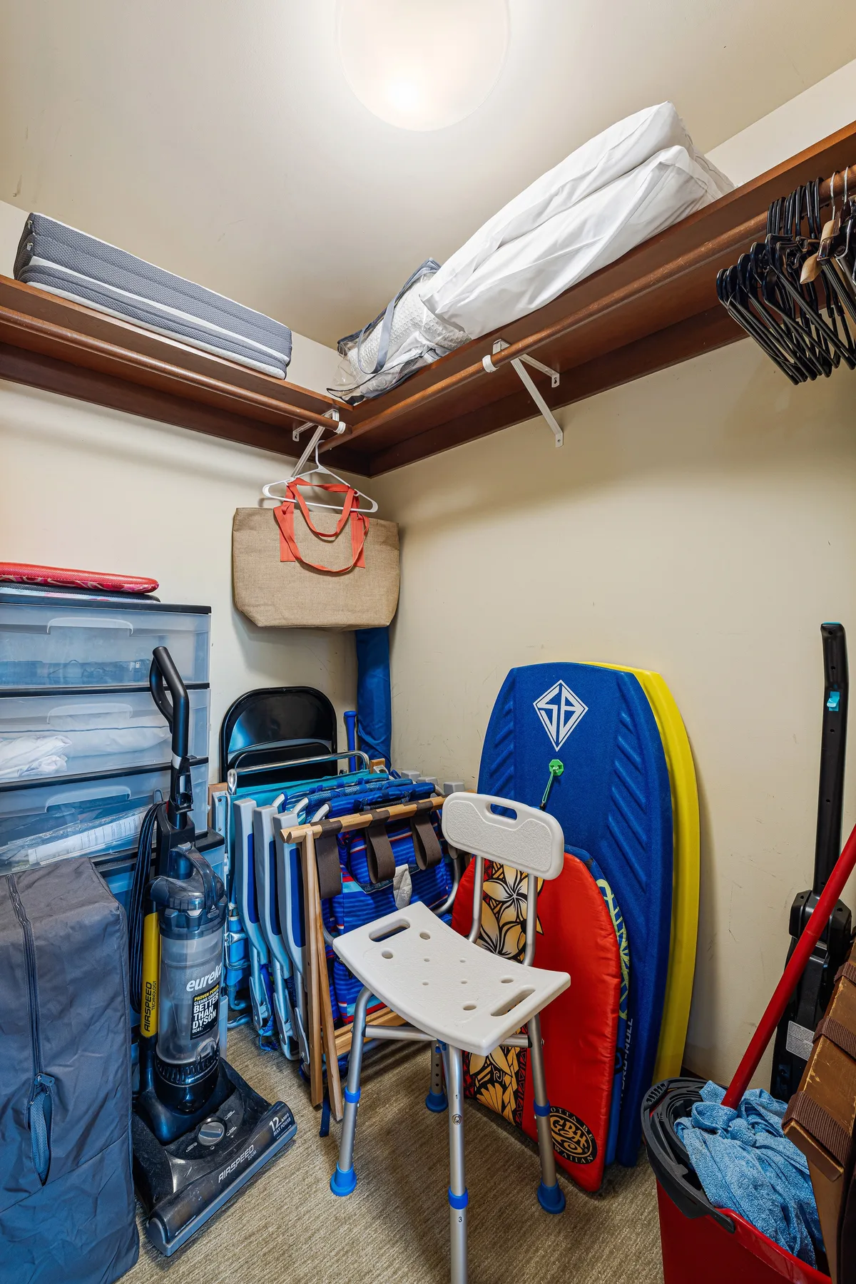 Un cuarto de almacenamiento con ropa doblada en estantes altos y diversos artículos debajo.