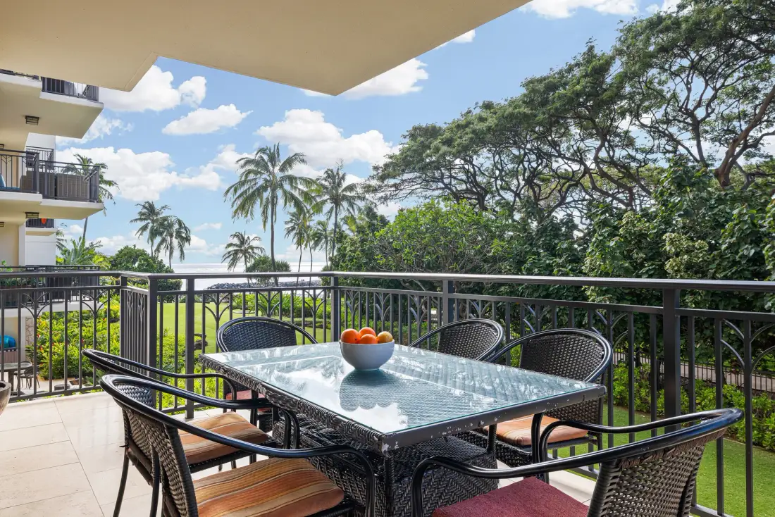 Comedor en un balcón con una mesa de vidrio y vistas a árboles y palmeras.