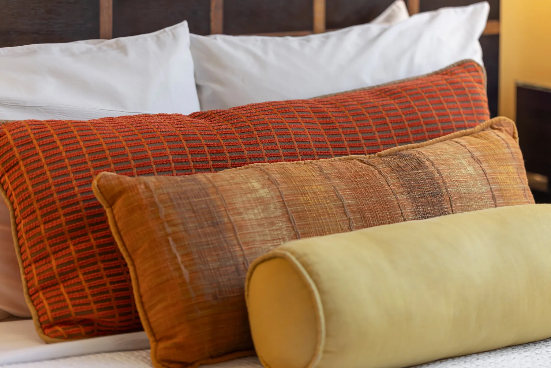 Una cama está adornada con almohadas estampadas superpuestas y un cojín cilíndrico.