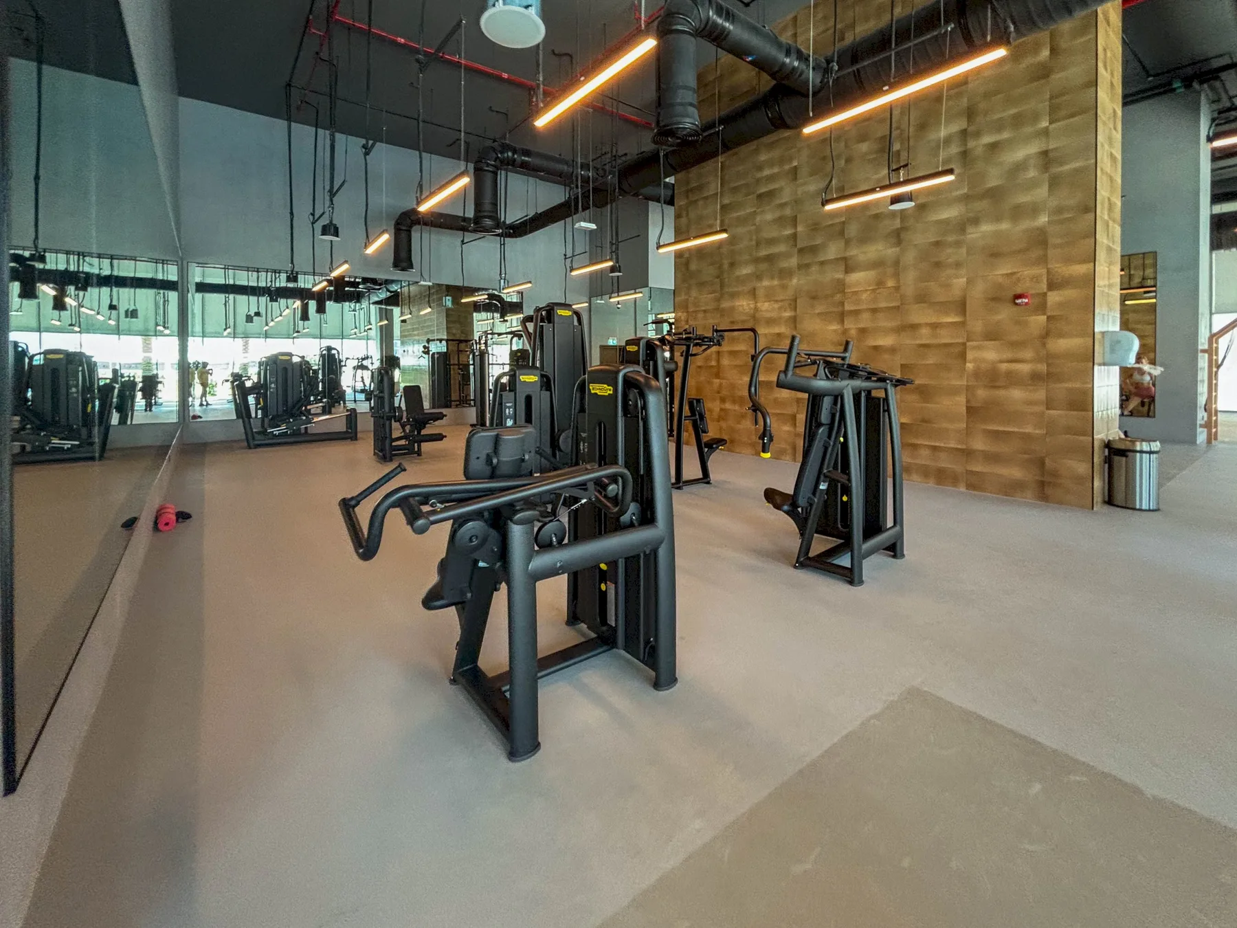 Un gimnasio con máquinas de ejercicio, paredes con espejos e iluminación en el techo.