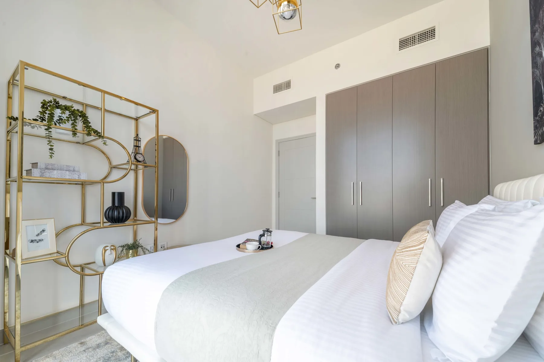 Un dormitorio con ropa de cama blanca y una estantería abierta dorada.