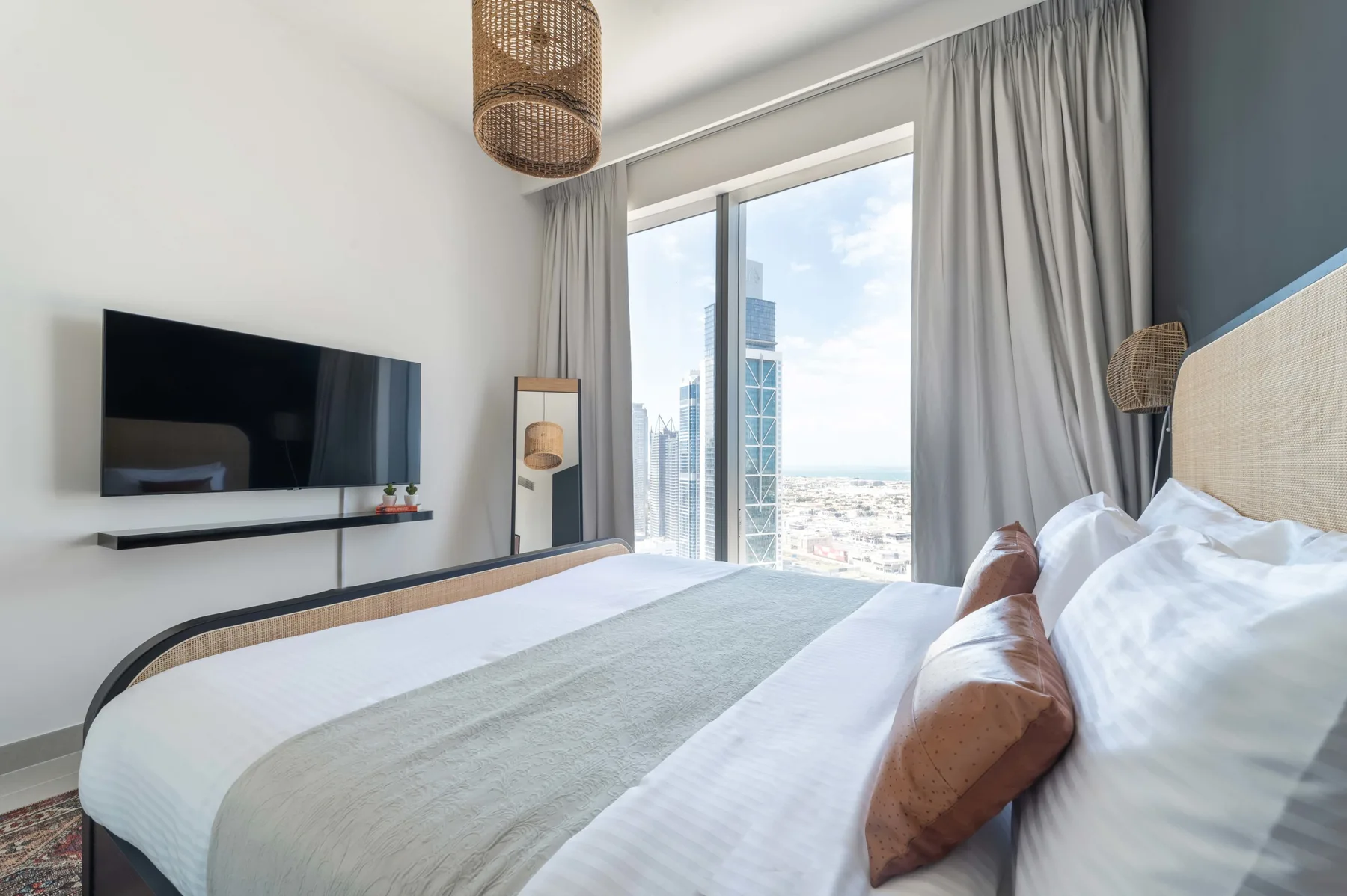 Un dormitorio luminoso con una cama grande junto a ventanales con vistas a la ciudad.