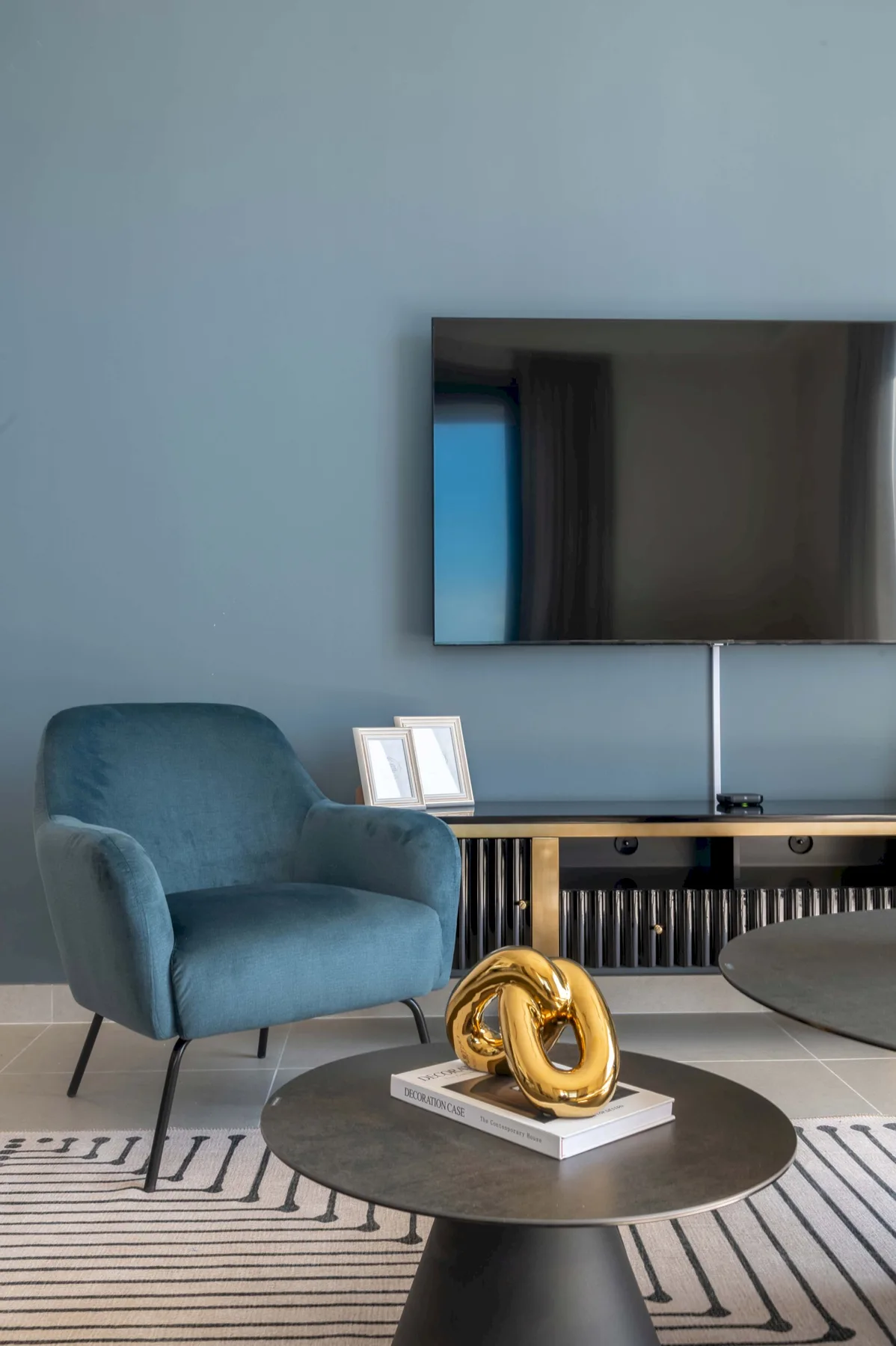 Una sala de estar moderna con un sillón azul, un televisor en la pared y una mesa de centro redonda.