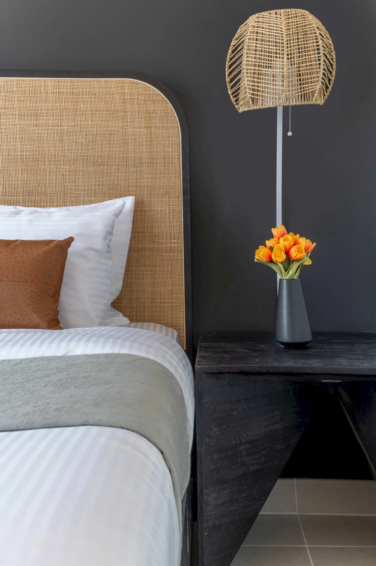 Un dormitorio con cabecero tejido, ropa de cama en capas y una mesita con flores.
