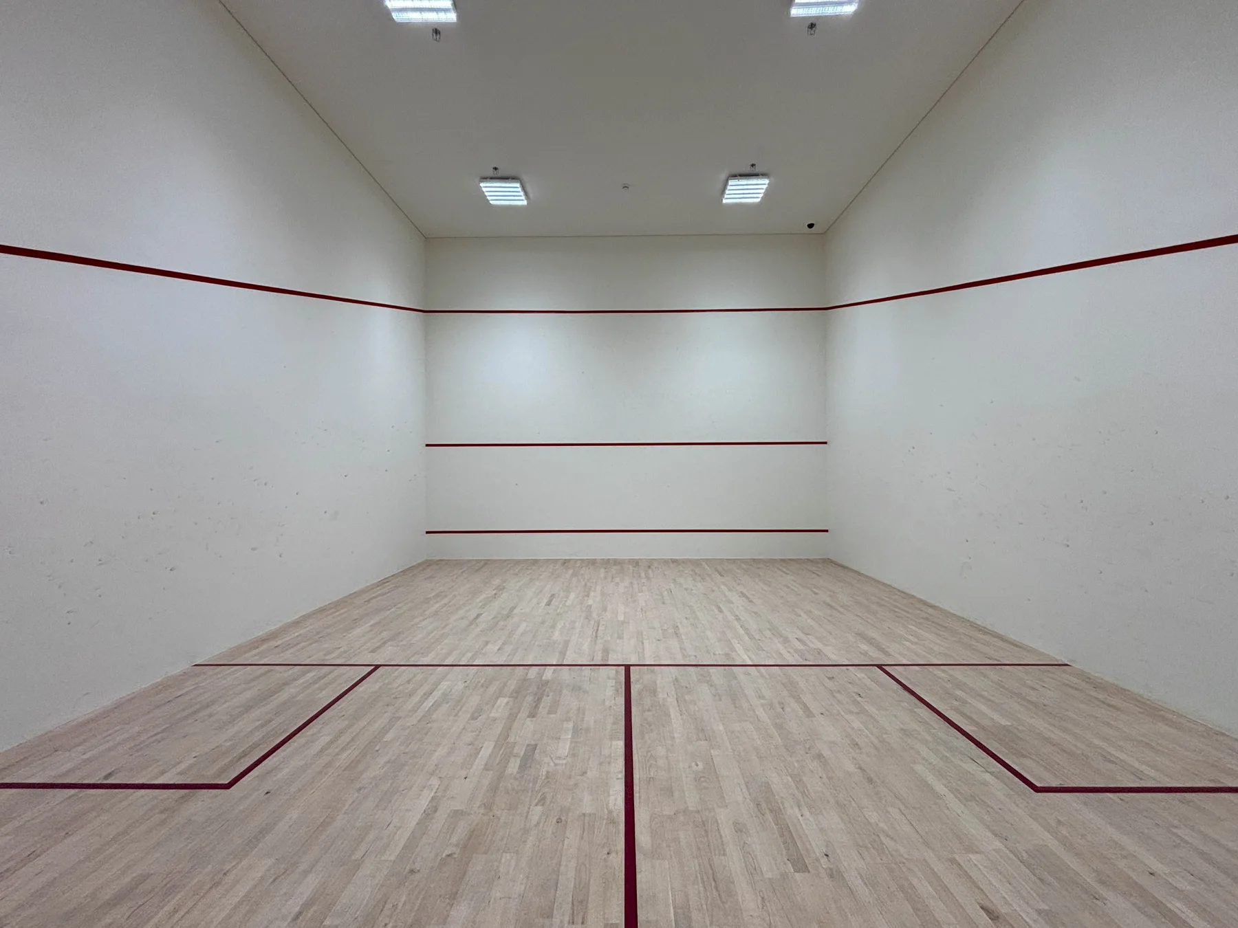 Una cancha cubierta con suelo de madera clara y líneas rojas.