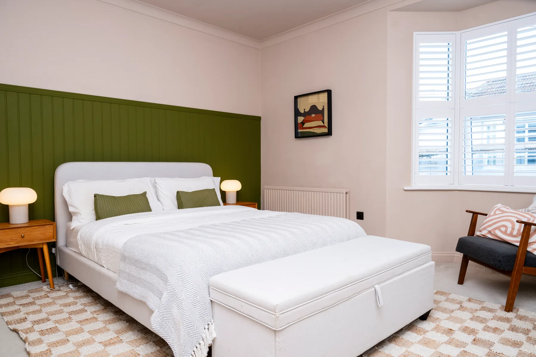 A bedroom with a white bed, green headboard, and large shuttered window.