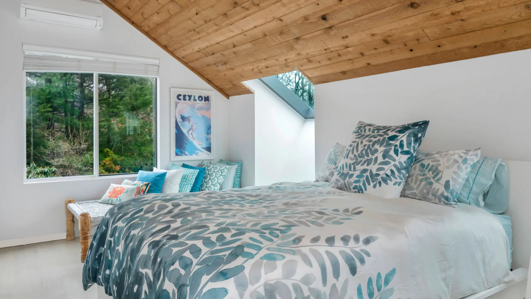 Un dormitorio con una cama grande vestida con ropa de cama estampada en tonos verdes y grises bajo un techo inclinado de madera.