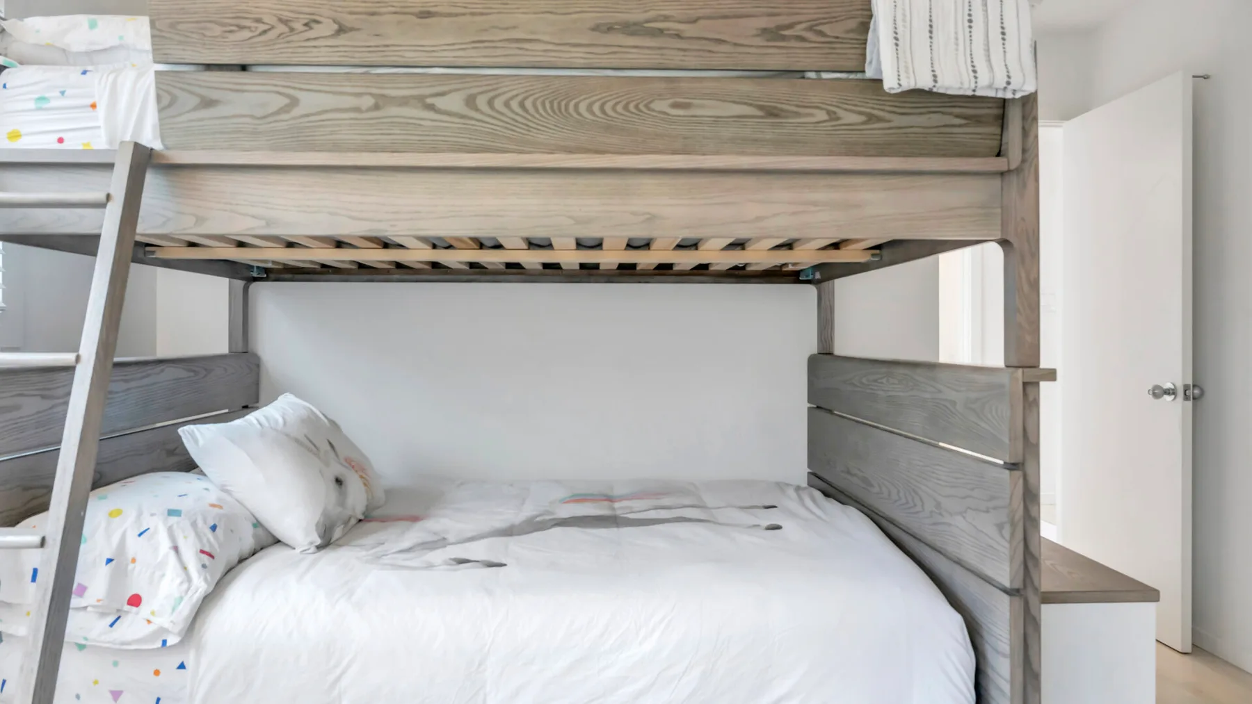 Una litera con ropa de cama blanca está junto a una pared clara.