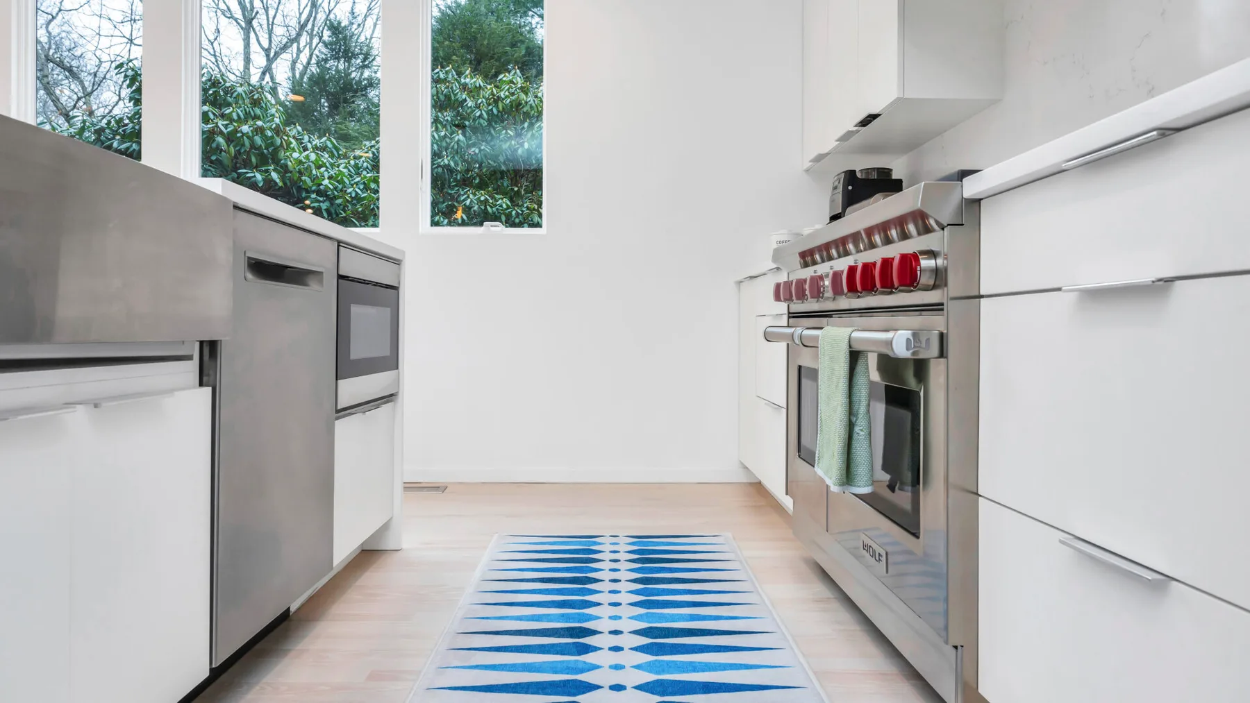 Una cocina luminosa con gabinetes blancos, electrodomésticos de acero inoxidable y una alfombra azul.