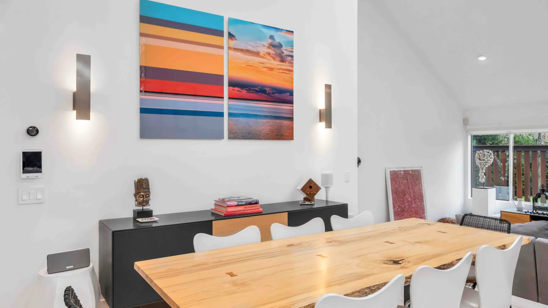 Un comedor luminoso con una larga mesa de madera bajo arte colorido en la pared.