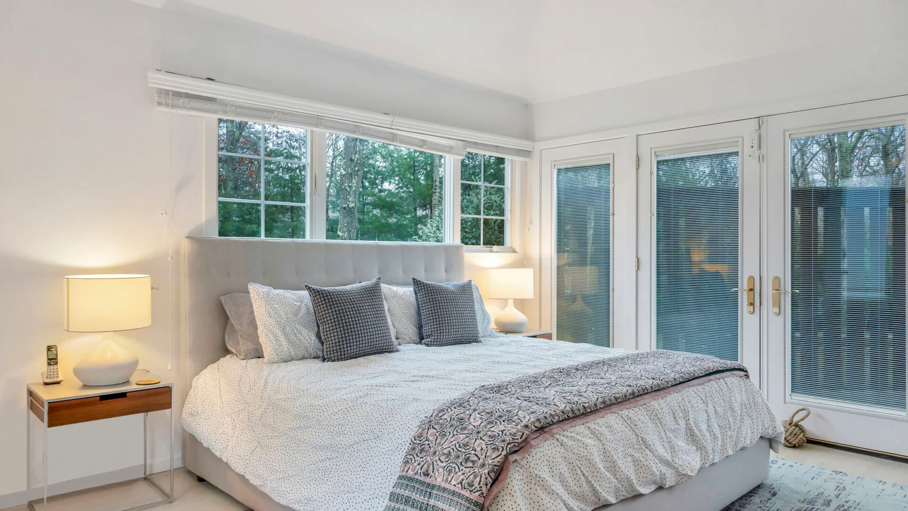 Dormitorio con una cama tendida junto a grandes ventanas y puertas de vidrio.