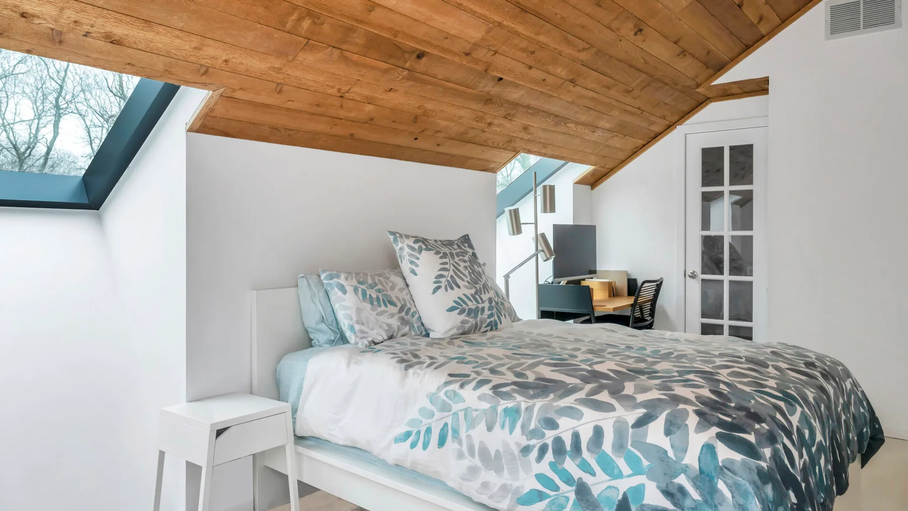 Un dormitorio con una cama bajo un techo inclinado de madera y una claraboya.