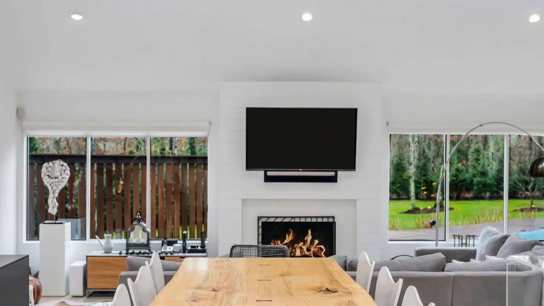Una luminosa sala de estar y comedor tiene una mesa larga de madera y un televisor sobre la chimenea.
