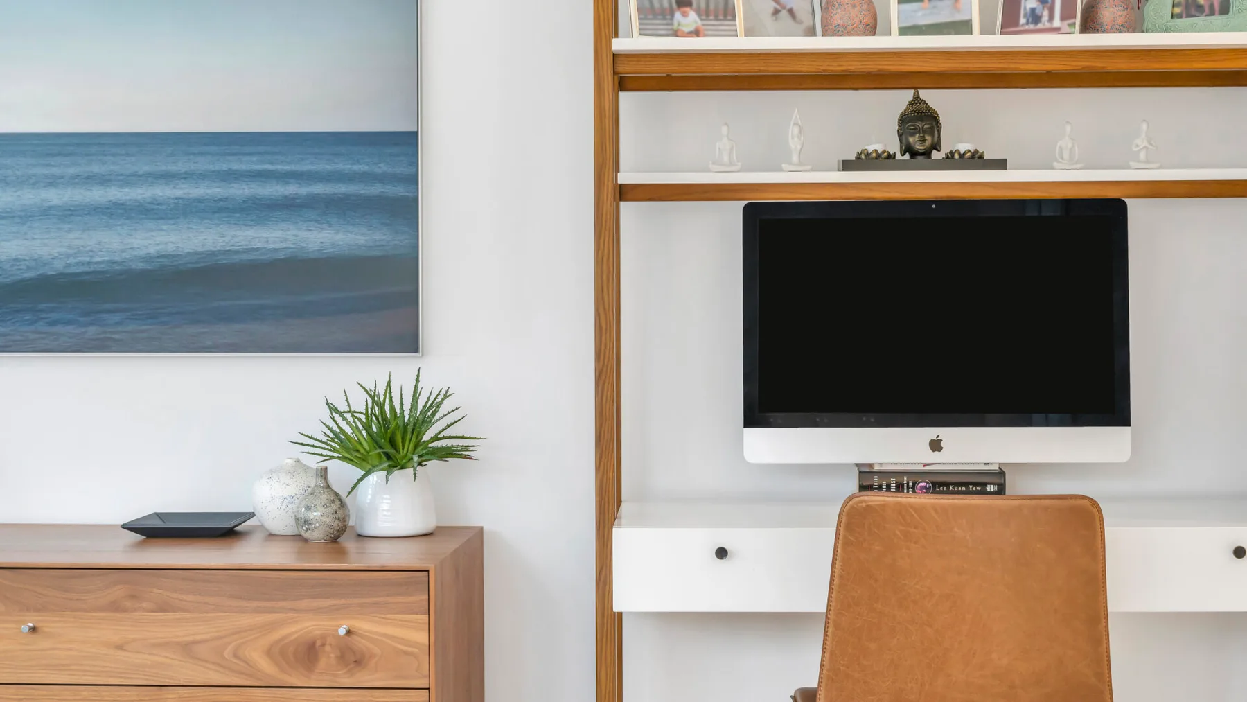 Un espacio de trabajo en un dormitorio con una computadora y una imagen enmarcada del mar.