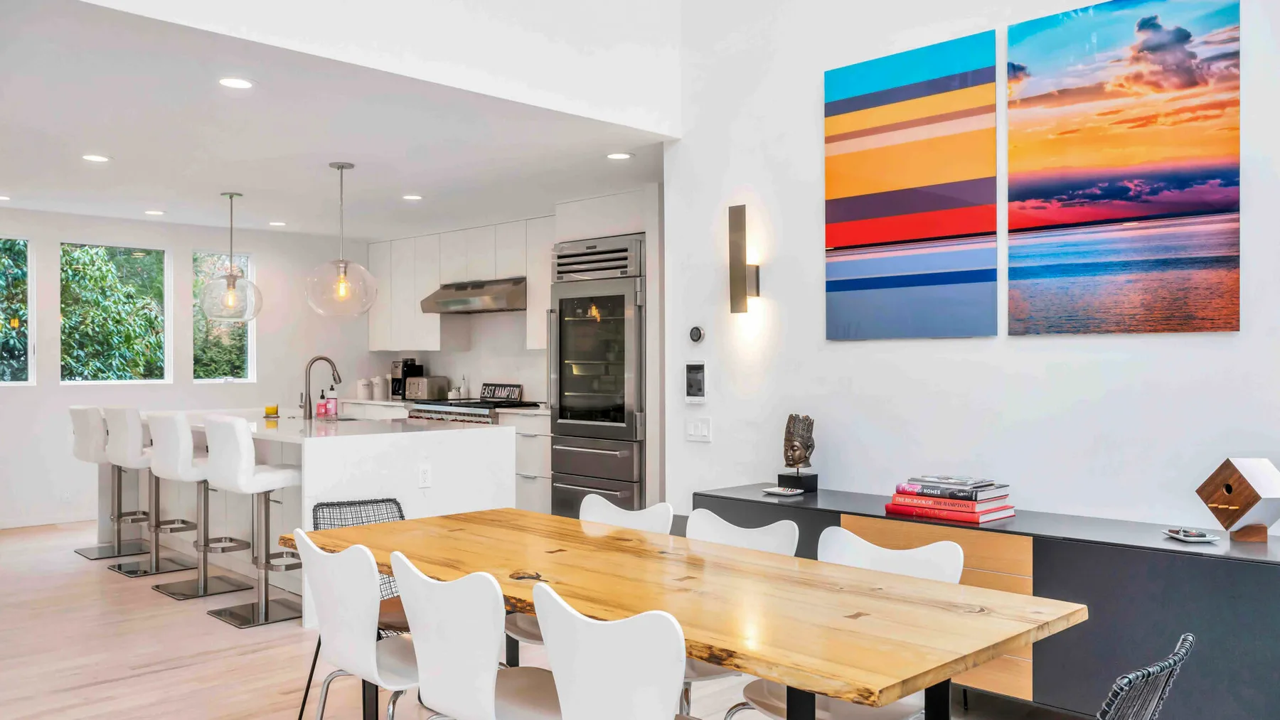 Una luminosa cocina abierta con comedor y una colorida imagen de atardecer en la pared.