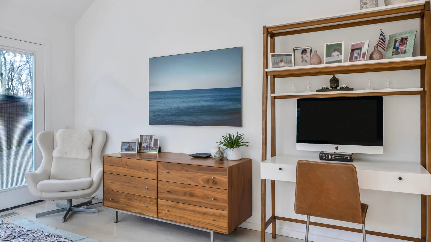 Una sala luminosa con una cómoda de madera, asientos blancos y un televisor.