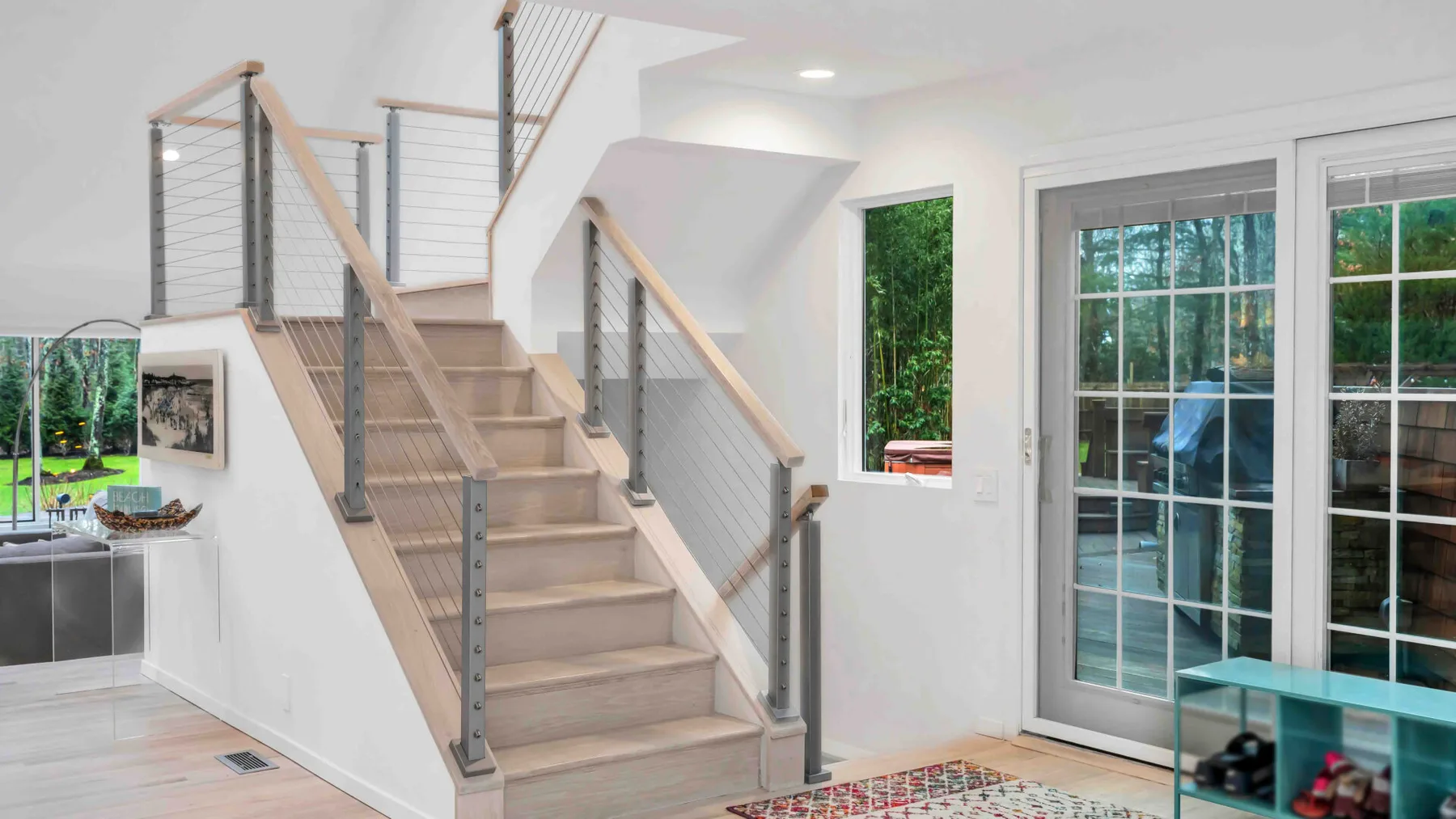 Un interior luminoso muestra una escalera junto a grandes ventanas y una puerta de vidrio.