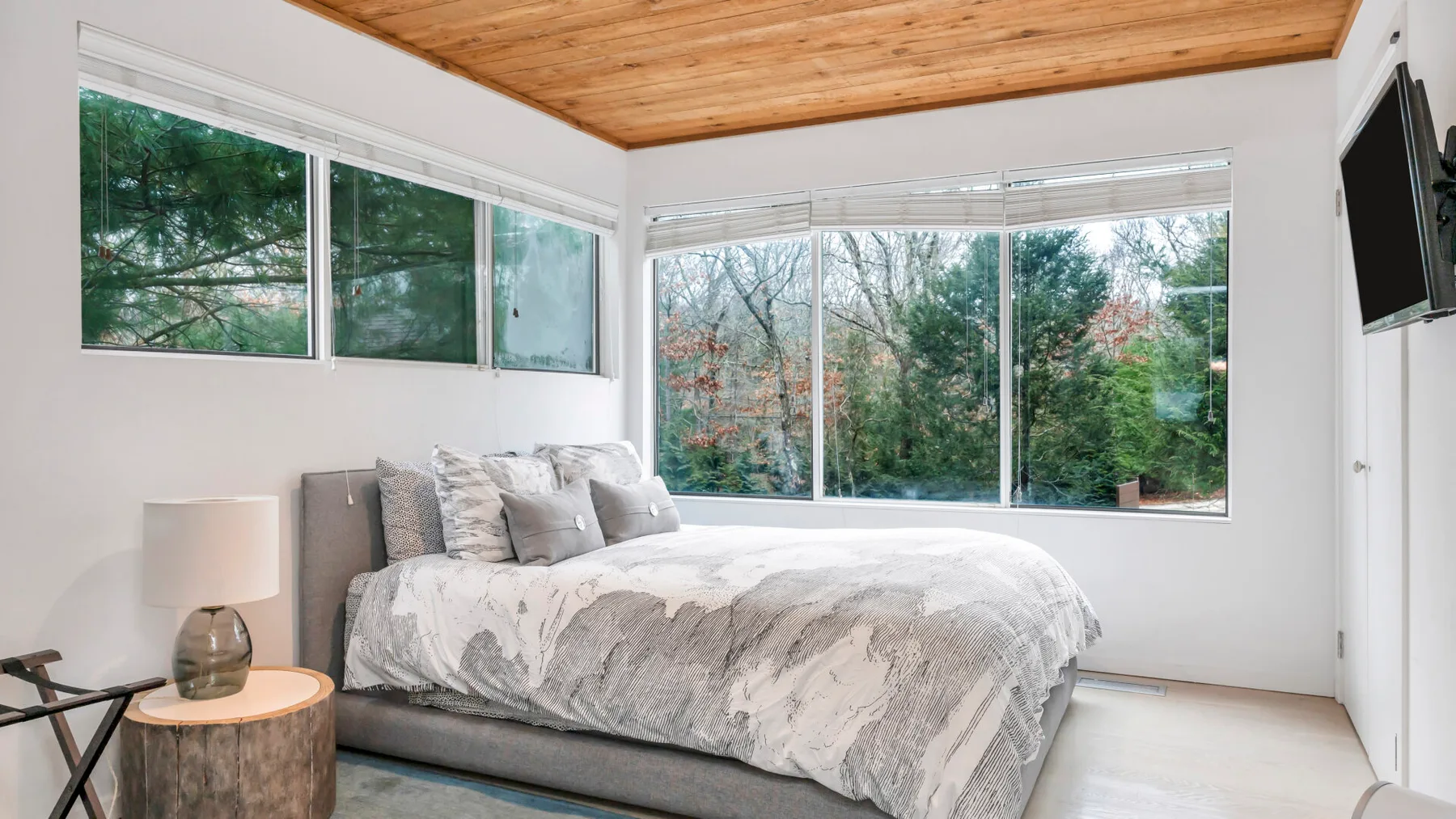 Dormitorio con una cama junto a grandes ventanas con vistas a los árboles.
