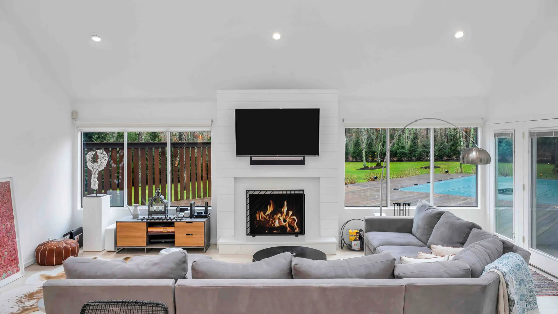 Una sala luminosa con asientos alrededor de una chimenea y grandes ventanas con vistas a una piscina.