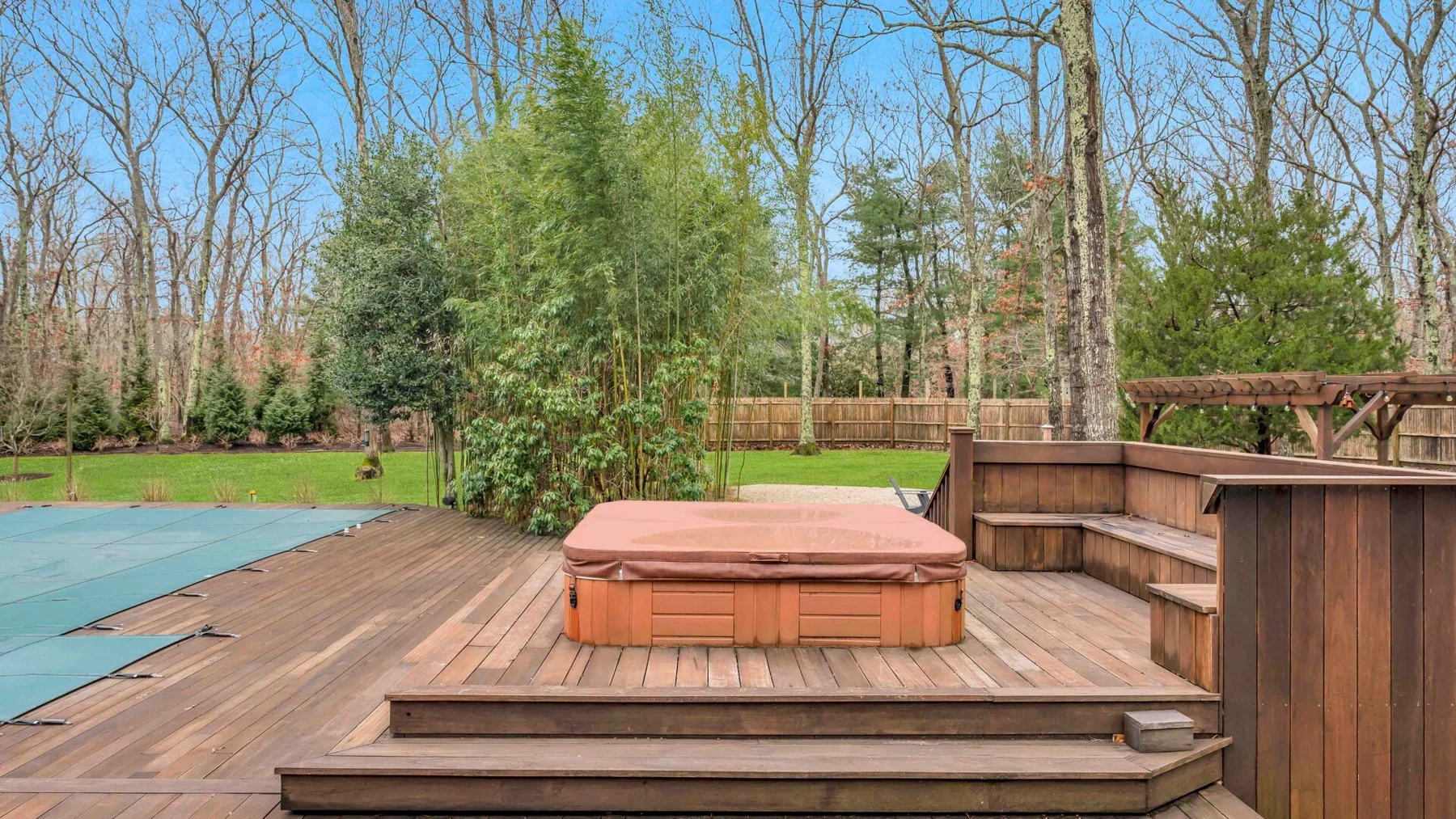Una terraza exterior de madera con una bañera de hidromasaje cubierta y asientos integrados.