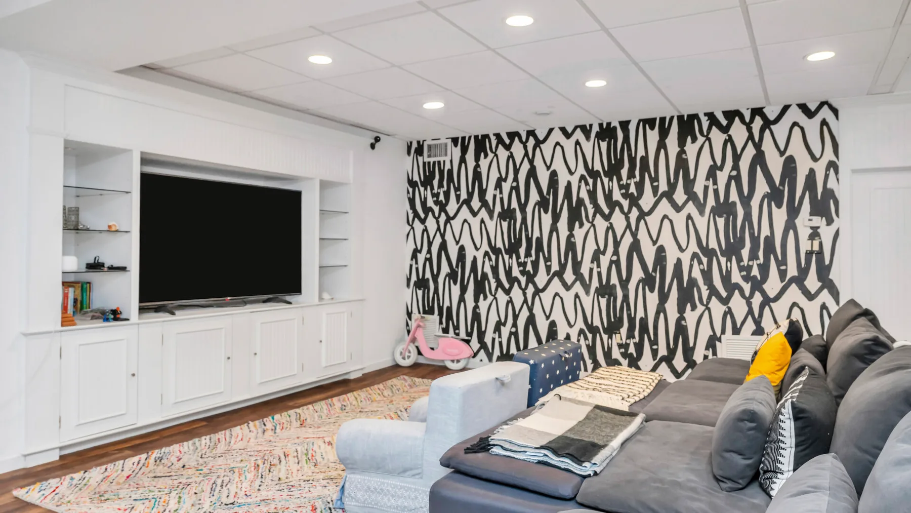 Una sala de estar con una amplia zona de asientos frente a un televisor y una pared estampada.