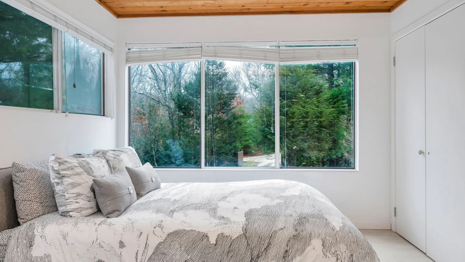 Un dormitorio con una cama junto a grandes ventanas con vistas a los árboles.