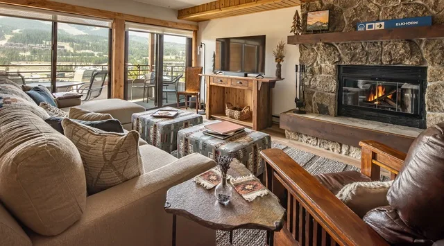 Una sala de estar con chimenea de piedra, asientos y grandes ventanas con vistas a las montañas.