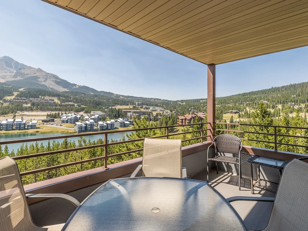 Una zona exterior cubierta con asientos ofrece vistas de colinas boscosas y una montaña.