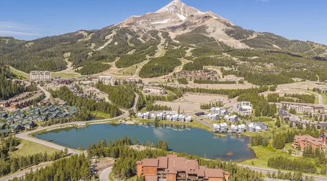 Una vista aérea muestra un complejo de montaña con un lago, laderas boscosas y una cumbre.