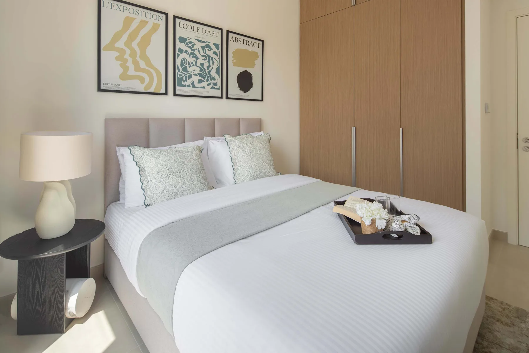 A bright bedroom with a neatly made bed and framed prints above the headboard.