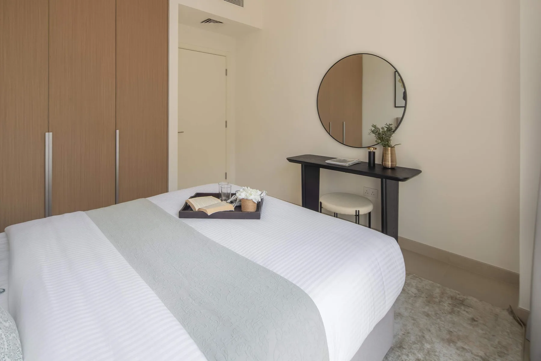 A bedroom with a neatly made bed and a round mirror above a console table.