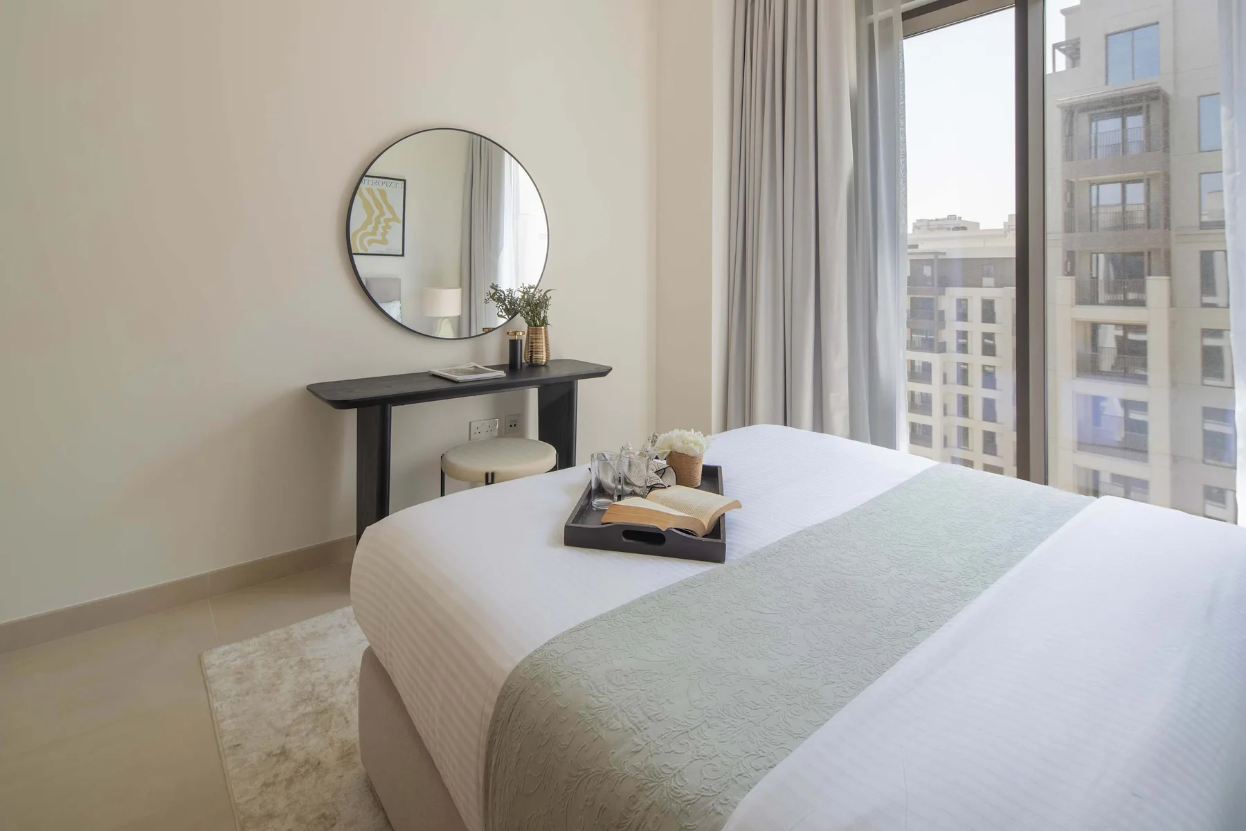 A bright bedroom with a neatly made bed beside a large window.