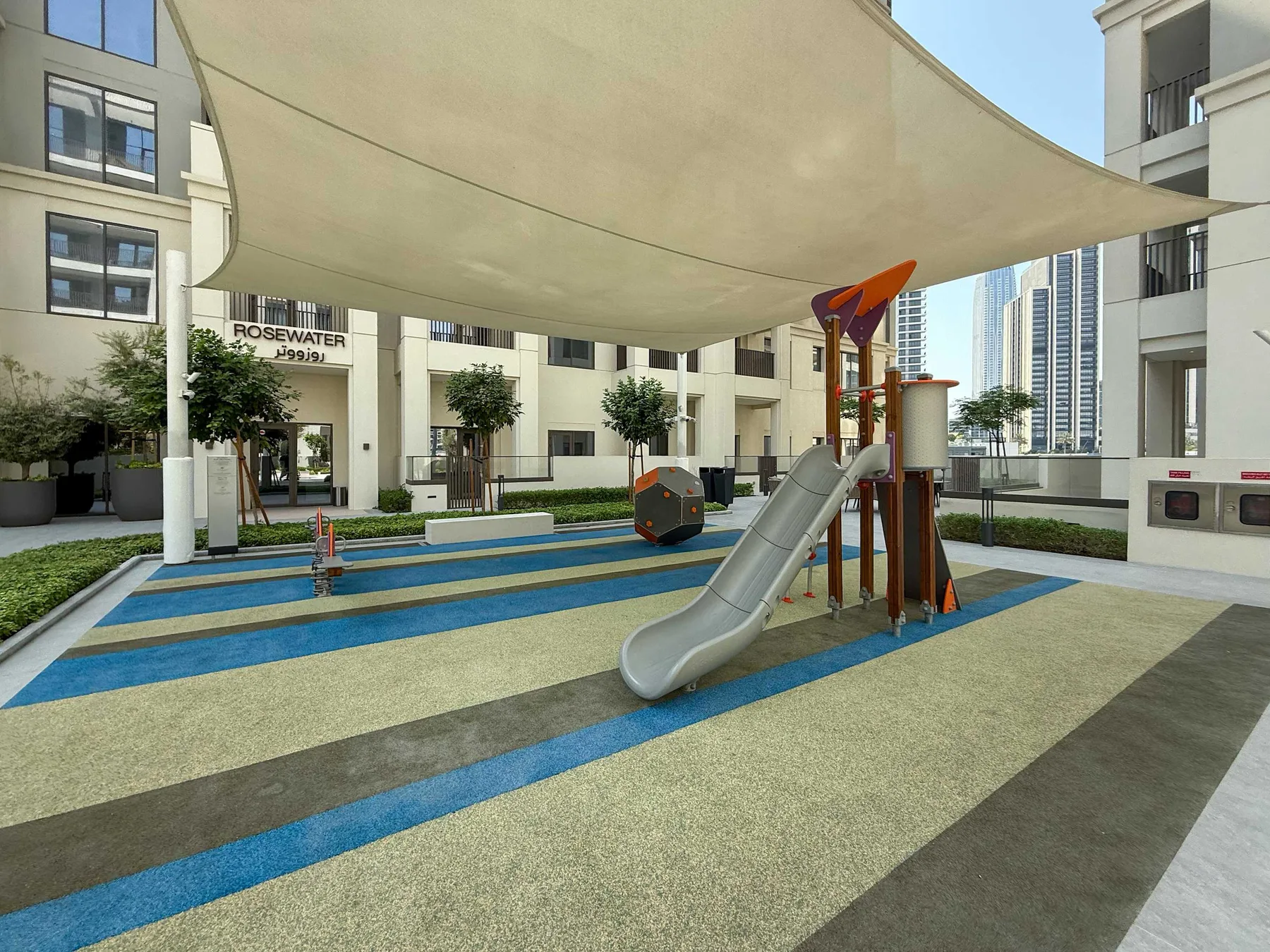 A shaded outdoor playground features a slide and colorful rubber surfacing.