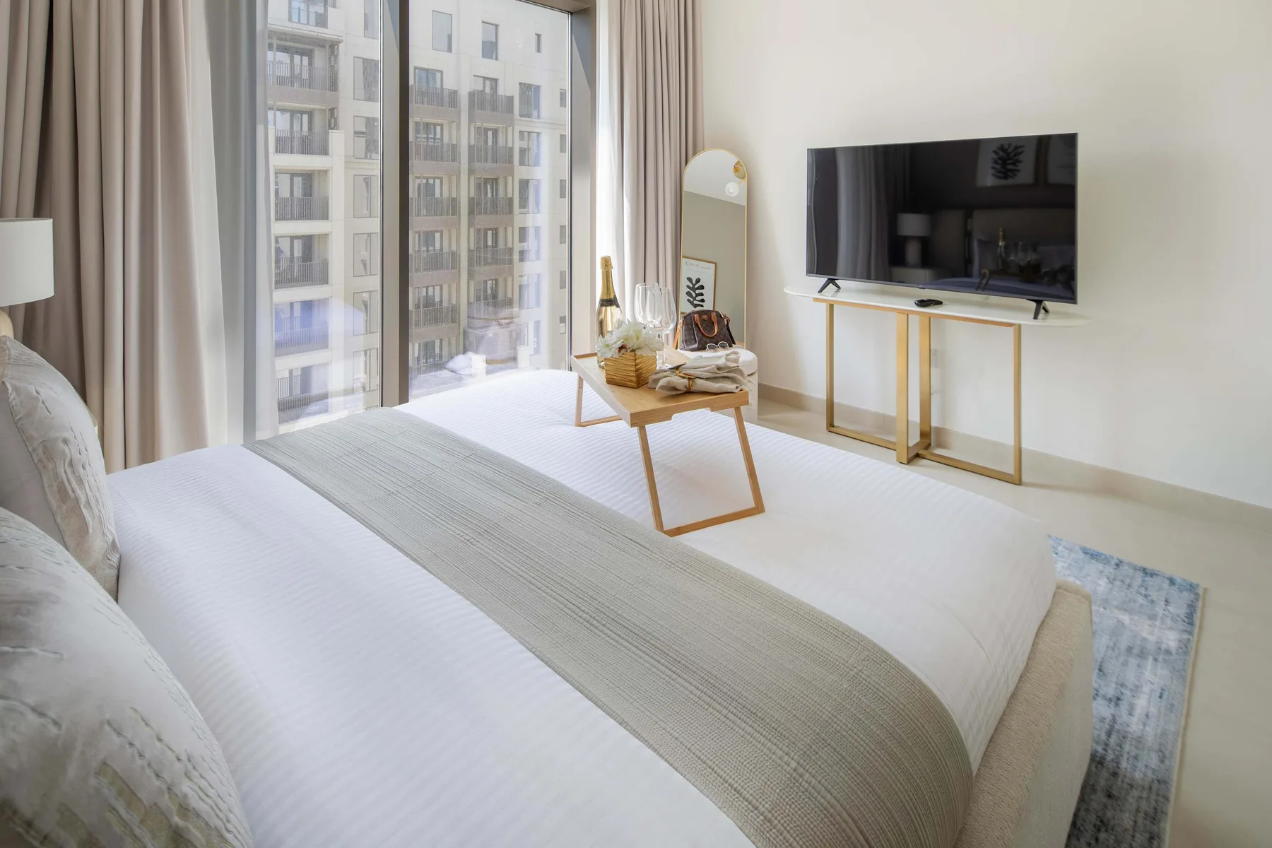 A bright bedroom with a bed, a television, and floor-to-ceiling windows.