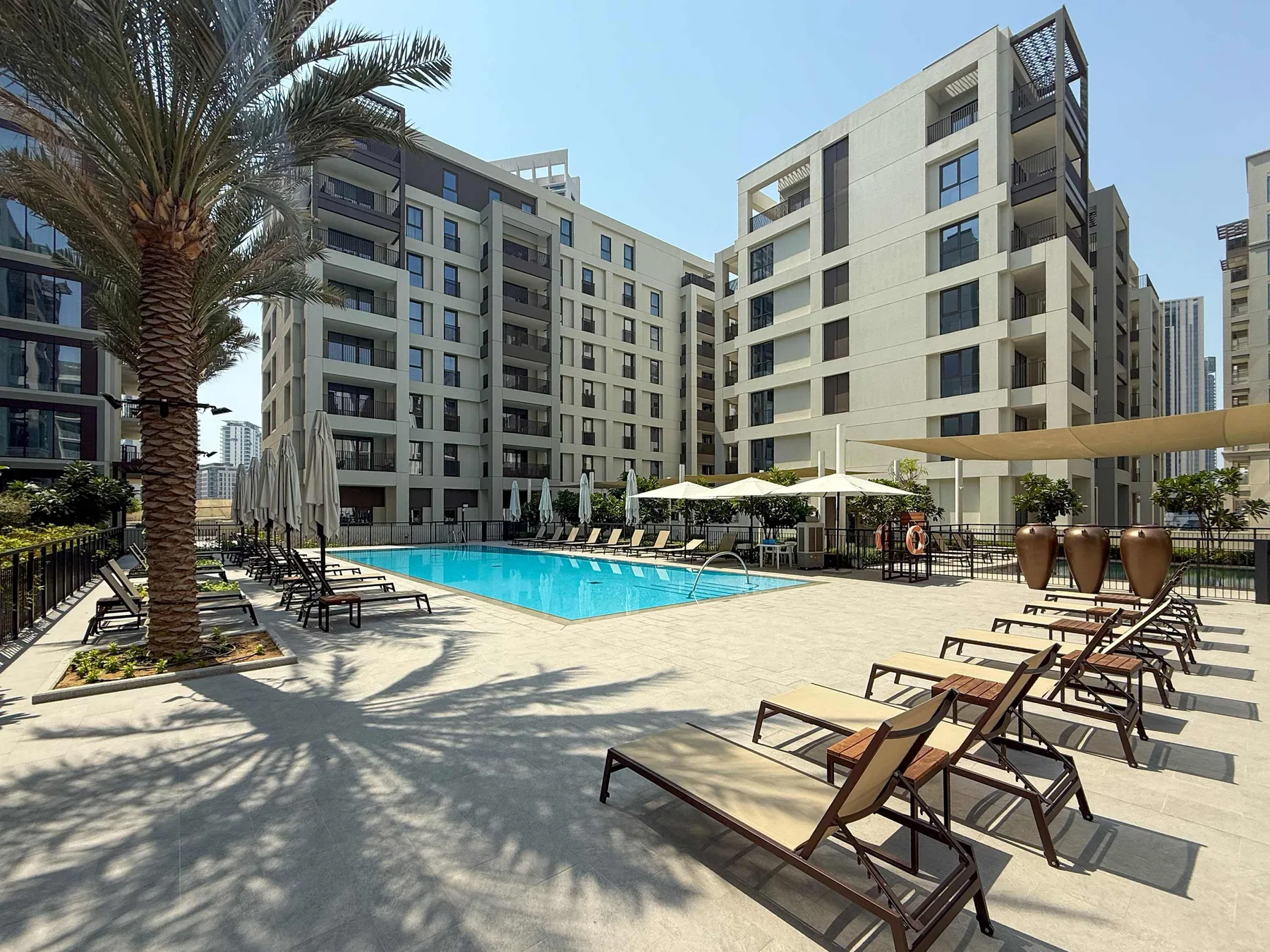 An outdoor swimming pool sits among modern apartment buildings and lounge seating.