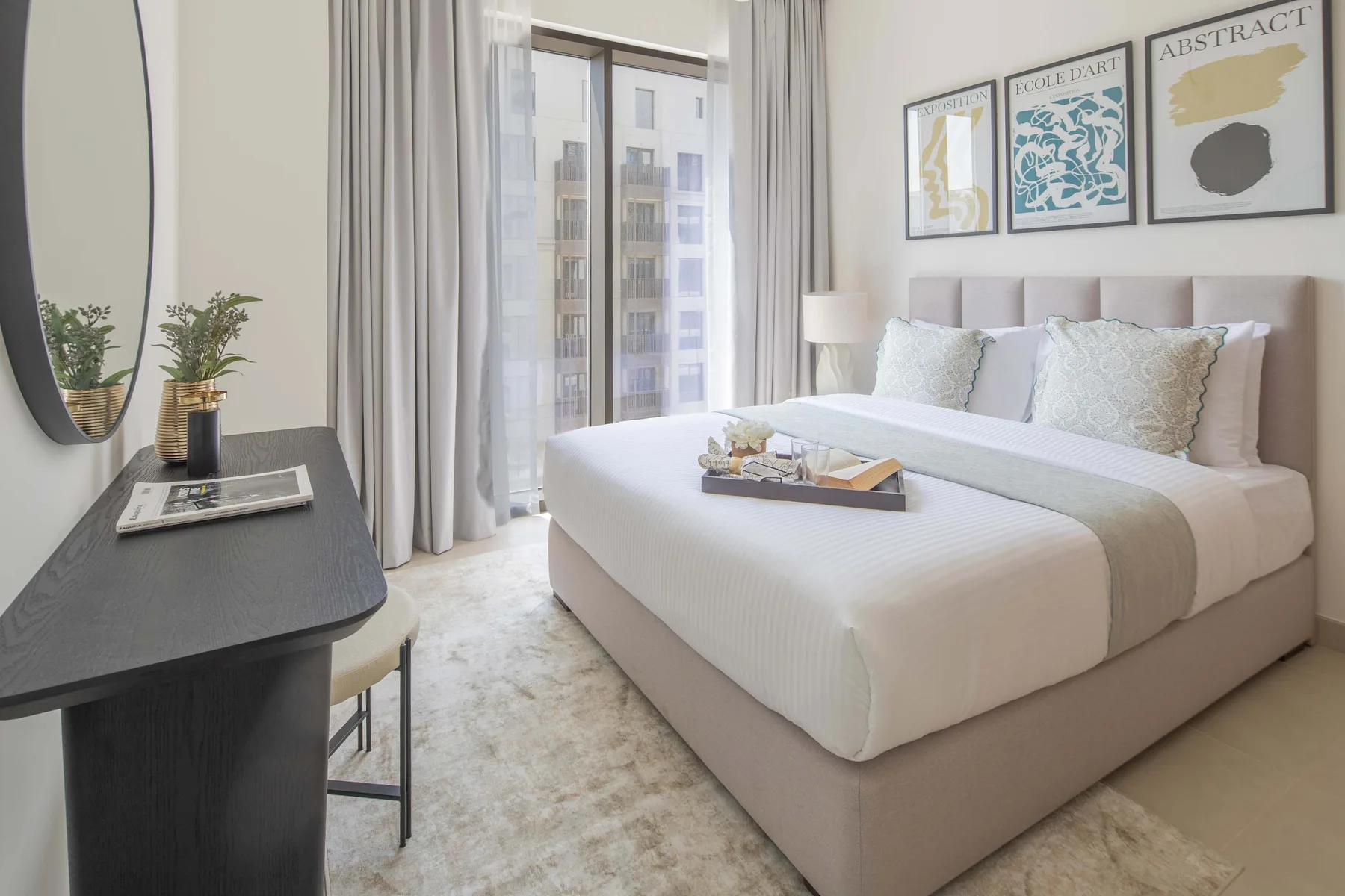 A bright bedroom with a neatly made bed and large curtained windows.