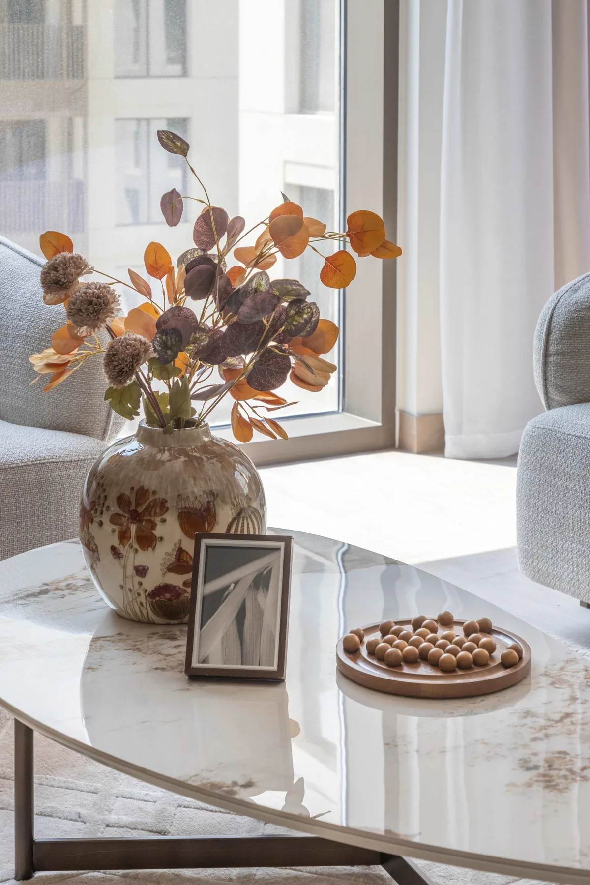 A bright living room with a coffee table, seating, and a vase of autumn leaves.