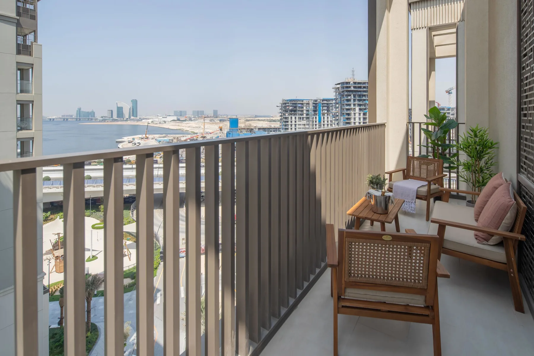 A balcony with wooden seating and potted plants overlooks the waterfront.