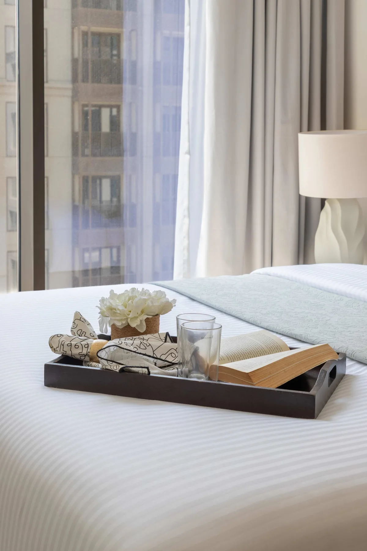 A bedroom with a neatly made bed and a tray of books and flowers.