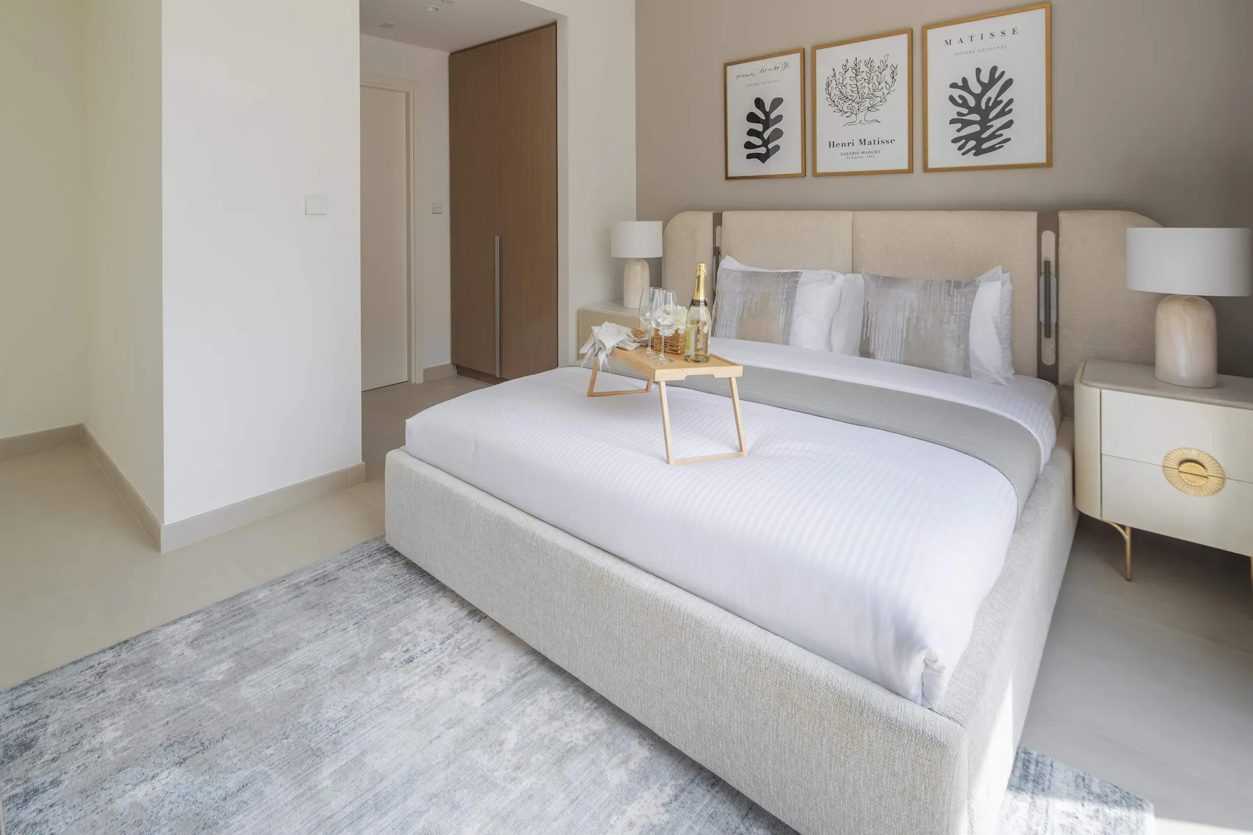 A bright bedroom features a large bed beneath three framed botanical prints.
