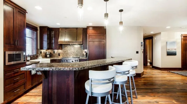A kitchen with a broad island, bar seating, and dark wood cabinets.