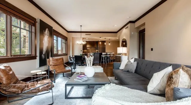 A bright living room with a seating area, large windows, and an open kitchen.
