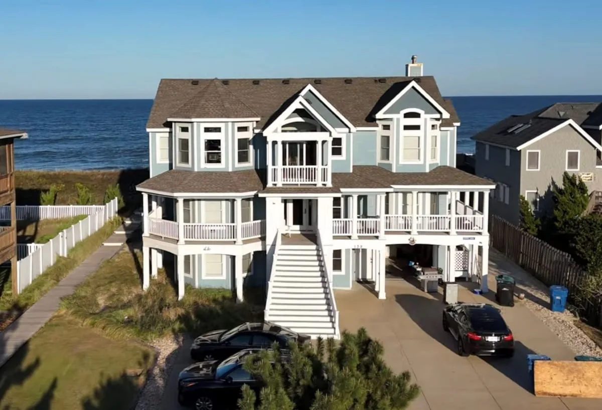 Una gran casa costera con porches blancos y una escalera da al océano.
