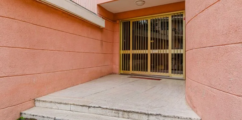 A recessed building entrance with barred glass doors and a short concrete approach.