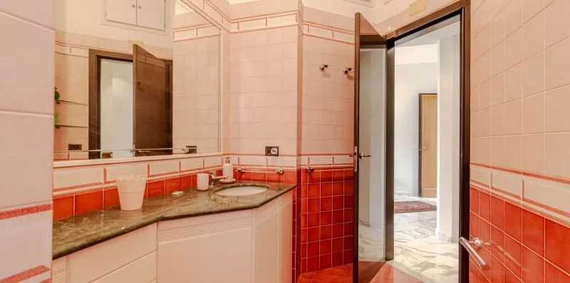 A tiled bathroom with a long sink counter and an open doorway.