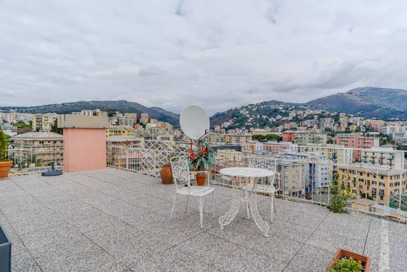 A rooftop terrace with outdoor seating overlooks a hillside city.