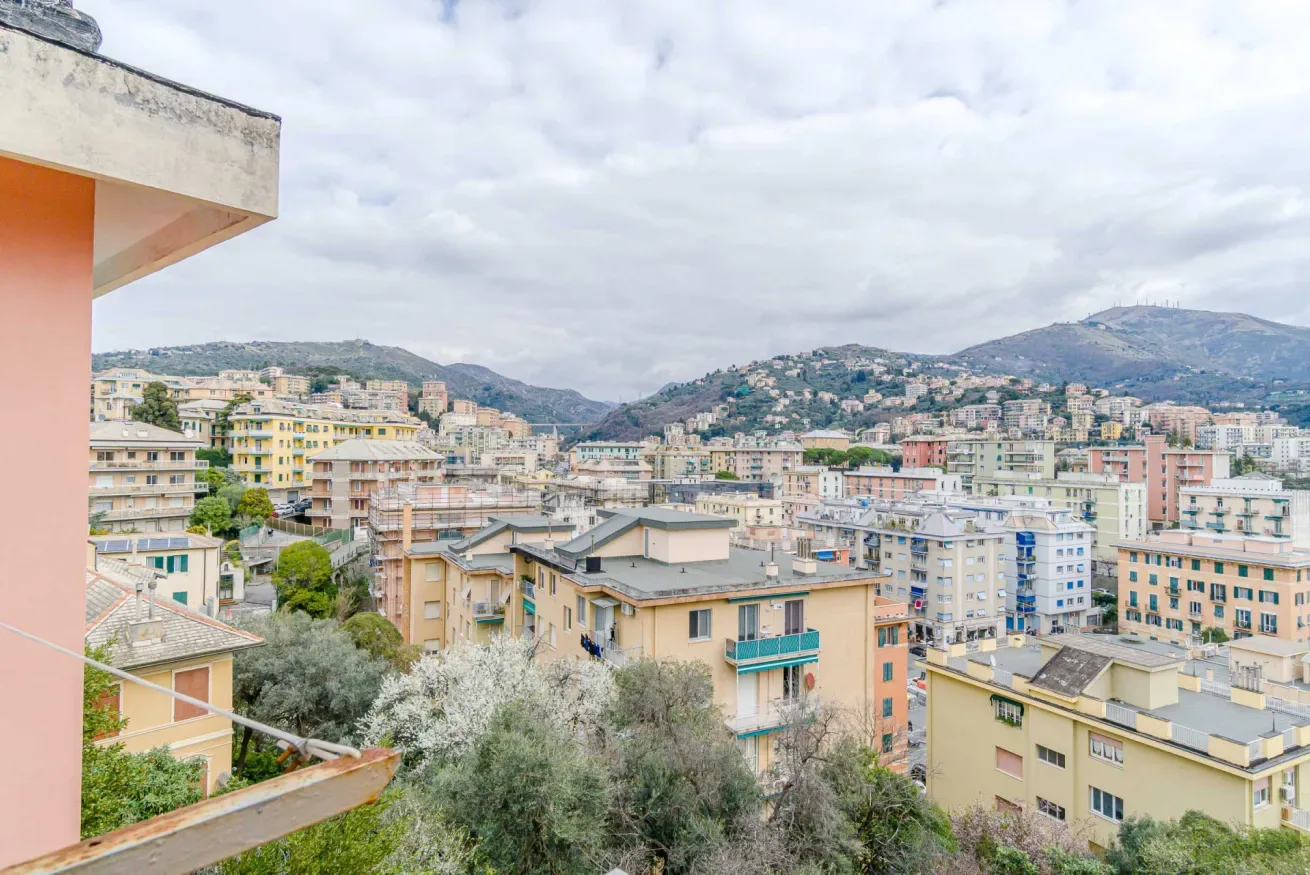 A cityscape of apartment buildings spreads across a valley beneath cloudy skies.