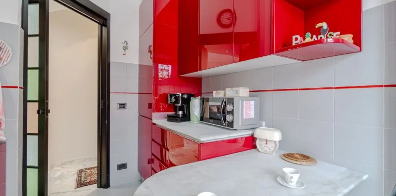 A compact kitchen with glossy red cabinets, countertop appliances, and a small dining surface.