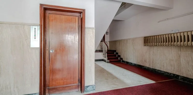 A building hallway with a wooden door beside a staircase.