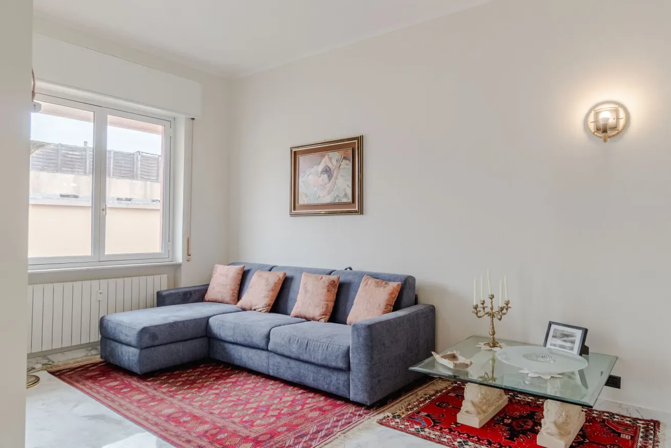 A living room with a blue sectional sofa, framed artwork, and a red patterned rug.